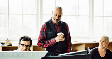 People working at desks and a person standing over their shoulder speaking to them