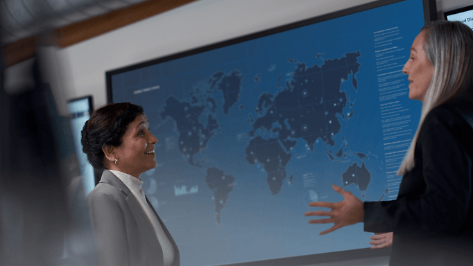 two people having a conversation in front of a large map on a screen behind them