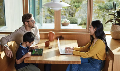 Eine Familie, die an einem Esstisch sitzt, sich unterhält und einen Laptop benutzt
