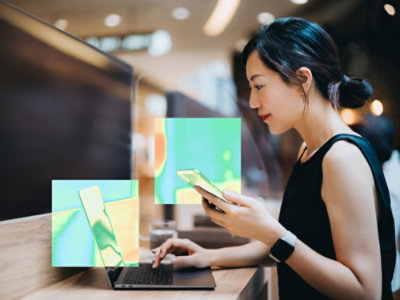 Nainen käyttää kannettavaa tietokonetta ja puhelinta.