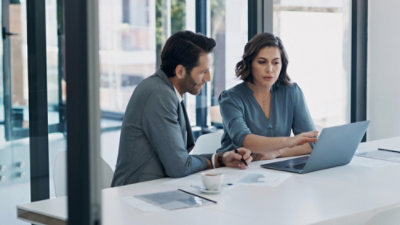 Two professionals reviewing information together on a laptop in an office.