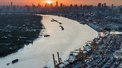 Container port and city skyline along a river at sunset.