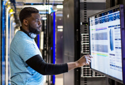 A person with headphones around his neck studying data on a large monitor