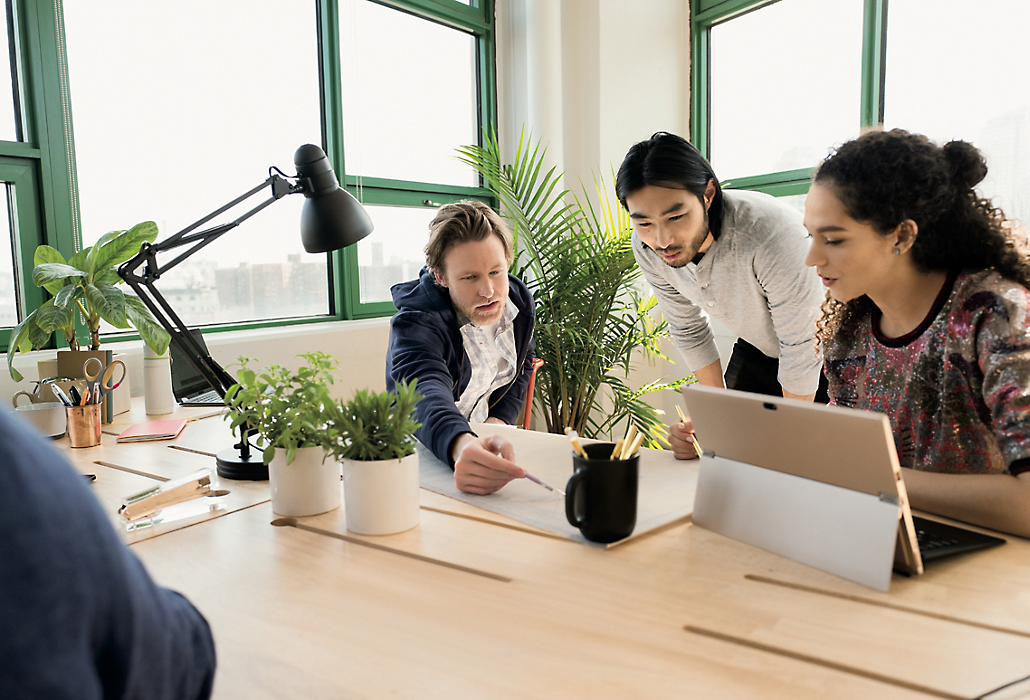 Tri osobe rade zajedno u jako osvijetljenom uredu. jedna koristi Surface Pro dok druge dvije razgovaraju o dokumentu na stolu