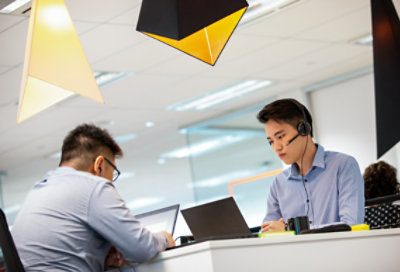 Two employees working on laptops at their desks. One is wearing a headset.