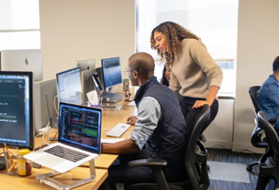 Un equipo de tres empleados que discuten una hoja de cálculo en un ordenador ante el escritorio de alguien más