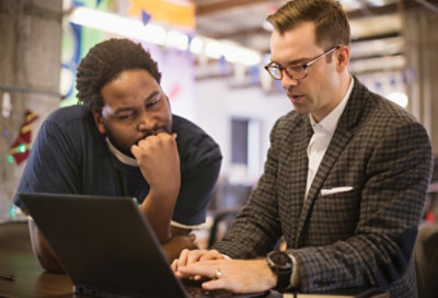 Two people standing at a raised table and looking at a laptop