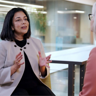 Two women sit and have a conversation in a modern office environment. 