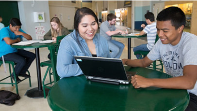 Two students sharing a table and laptop in a school