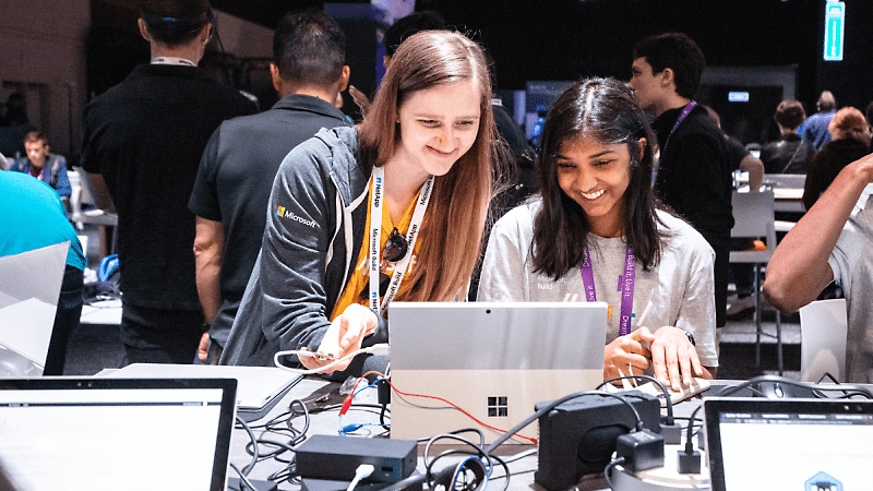 Dois estudantes a sorrir e a trabalhar em conjunto num dispositivo Surface.