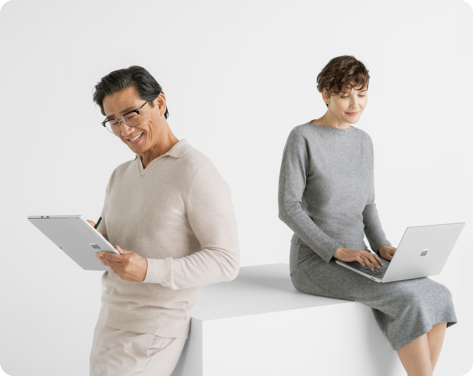 Two adults work on their devices against a white background. One stands with a tablet and stylus