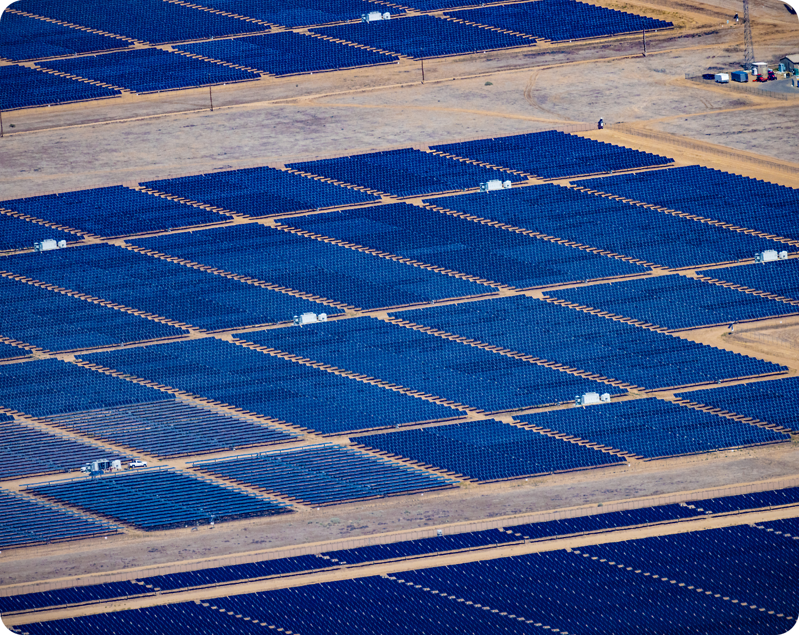 Aerial view of a large solar farm in a desert, featuring extensive rows of blue solar panels arranged in a grid pattern