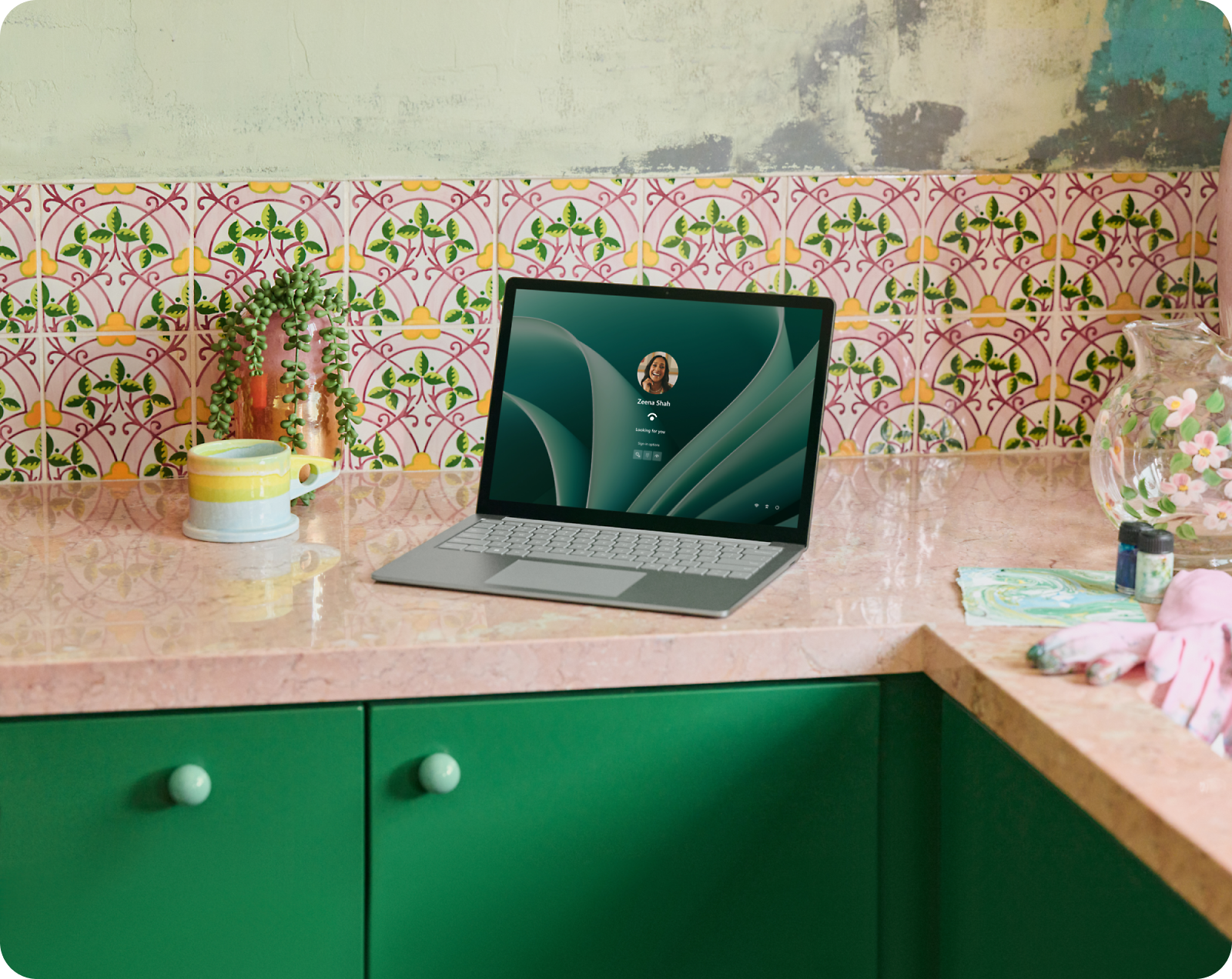 A laptop with a login screen sits on a pink marble kitchen counter, surrounded by colorful patterned tiles