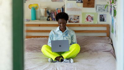 A person uses Surface Laptop Go while sitting on her bed.
