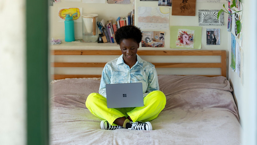 A person uses Surface Laptop Go while sitting on her bed.