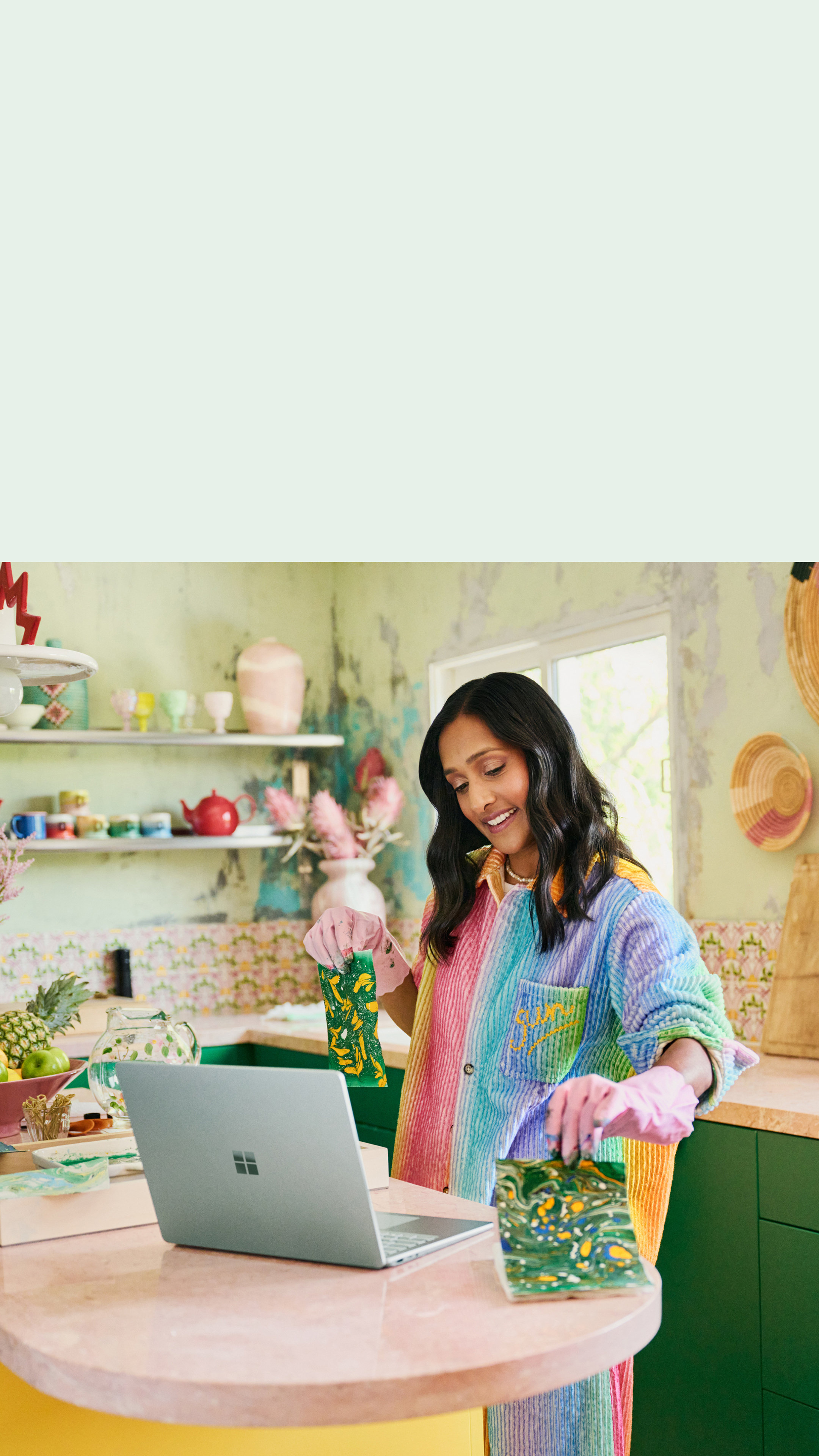 A woman stands at a worktop holding crafts she made in front of the camera of her Surface Laptop 5.