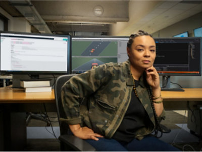 Eine Person, die an einem Schreibtisch mit mehreren Monitoren sitzt und ihr Kinn auf ihre Hand stützt