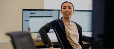 A person seated at a desk with dual monitors, turning to look over their shoulder in an office setting.