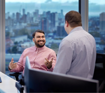 Twee mannen die in gesprek zijn in een kantoor met grote vensters met uitzicht op een stadslandschap. 