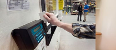 A person in a plaid shirt uses a card to clock in at a time-tracking device.