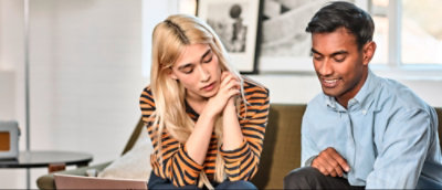 Two people sitting together on a couch. The person on the left has blonde hair and is wearing a striped shirt.