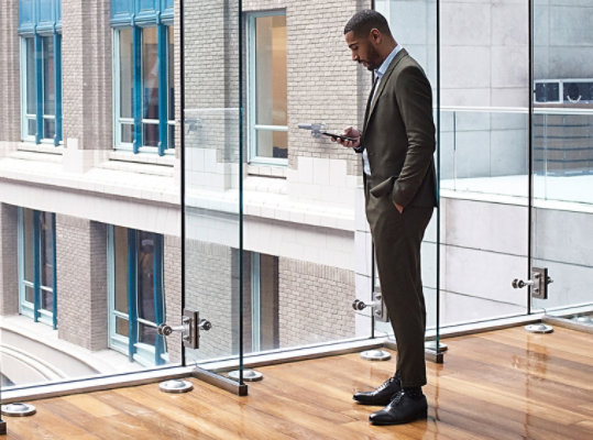 A person using a mobile phone standing in front of a large wall of windows.