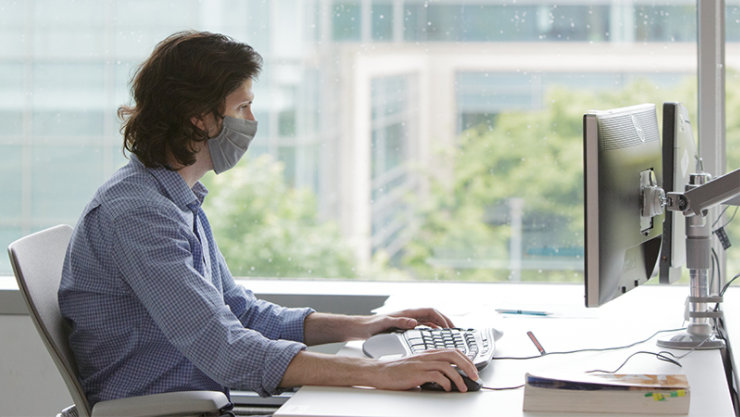 A male employee wearing a face mask and working at his desk.