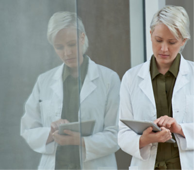 A woman in a white lab coat using a tablet.
