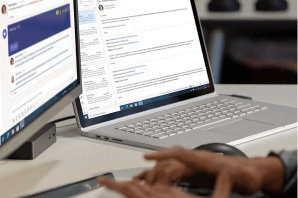 A laptop connected to a desktop monitor and hands typing on a keyboard 