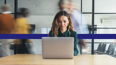 Person working on a laptop in a busy office environment. Image from the IDC white paper.