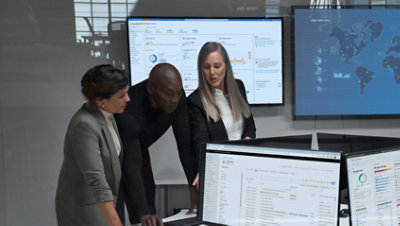 Drei Personen, die sich über einen Schreibtisch beugen und auf einen Monitor schauen