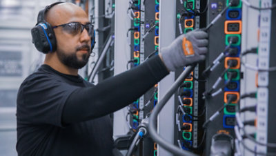 Uma pessoa com óculos e auscultadores de proteção a trabalhar com cabos numa sala de servidor