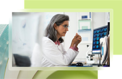 Une femme en blouse blanche regardant un écran d’ordinateur.