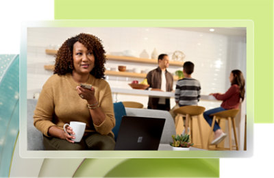 A woman holding a phone and looking at a laptop.
