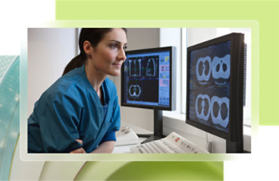 A woman in scrubs looking at computer screens.