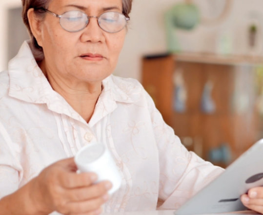 Older adult looking at a bottle of medication and holding a tablet device.