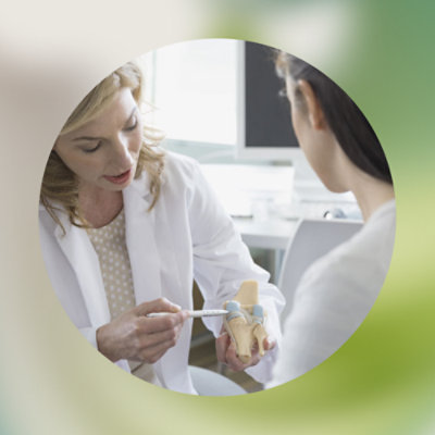 A woman in a white coat holding a model of a human foot.