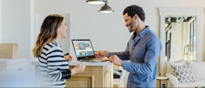 Two individuals standing at a kitchen island with an open laptop and documents, engaged in a discussion.