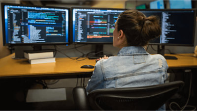 A person working at their desk with multiple screens.