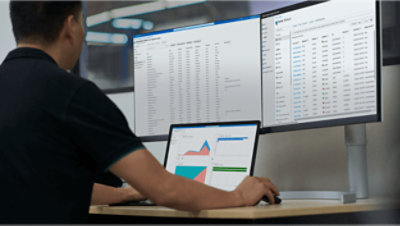 A person working at their desk on a laptop and two monitors.