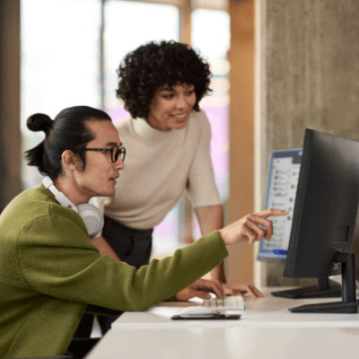 Dua orang melihat desktop dan satu orang menunjuk layar dengan jari