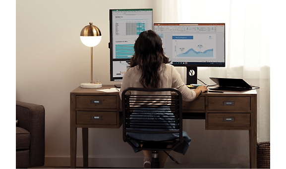A woman is sitting on chair and working with multiple screens.