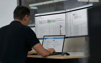 Seseorang sedang bekerja menggunakan laptop dengan dua monitor tambahan