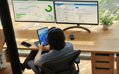 Seseorang menggunakan tablet. Grafik dan layar email dibuka di dua monitor yang ada di meja.