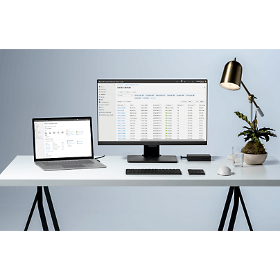 Laptop e desktop sono posizionati su un tavolo con alcuni report aperti e una lampada da tavolo accanto.
