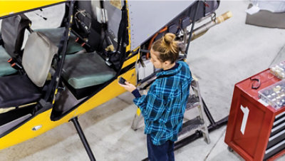 Seseorang berdiri di depan mesin besar menggunakan perangkat genggam yang tergantung di leher.