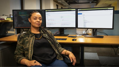 Seseorang duduk di depan mejanya dengan beberapa layar yang menampilkan kode. 