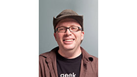 A Person smiling, wearing a brown jacket over a black T-shirt.