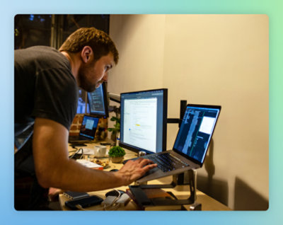 두 대의 컴퓨터가 있는 책상에 앉아 있는 한 사람