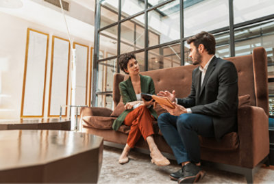 Two people sitting on a sofa in a modern office lobby, engaged in a conversation.